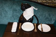 Cat sculpture wearing napkin at a laid table